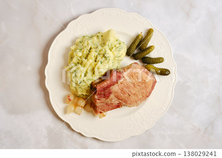 Enjoying a pork rib chop meal with mashed potatoes and pickles on a white plate 138029241