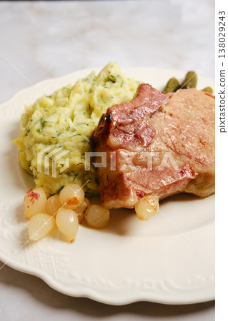 Pork rib chop served with mashed potatoes and pickles on a white plate with a side of onions Pork rib chop served with mashed potatoes and pickles on a white plate with a side of onions 138029243