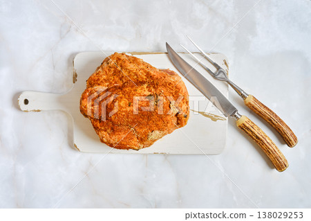 Looking at a pork shoulder on a cutting board with carving tools on a light surface Looking at a pork shoulder on a cutting board with carving tools on a light surface 138029253