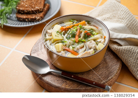 Chicken noodle soup with fresh dill in a bowl on a yellow kitchen tile background Chicken noodle soup with fresh dill in a bowl on a yellow kitchen tile background 138029354