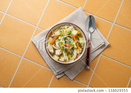 Chicken noodle soup with fresh dill in a bowl on a yellow kitchen tile background Chicken noodle soup with fresh dill in a bowl on a yellow kitchen tile background 138029355