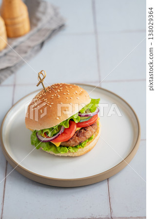Meat burger with tomato, cheese, and lettuce on a plate on a kitchen table with spice and napkin. Meat burger with tomato, cheese, and lettuce on a plate on a kitchen table with spice and napkin. 138029364