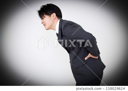 一位身穿西裝的中年商人,正遭受腰痛的困擾。 一位身穿西裝的中年商人,正遭受腰痛的困擾。 138029624