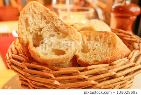 Slices of fresh baguette in a wicker basket on a table, representing French cuisine and European dining 138029692