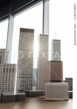 A collection of miniature building models arranged on a wooden surface, set against a bright window backdrop, creating a sense of urban scale 138029887