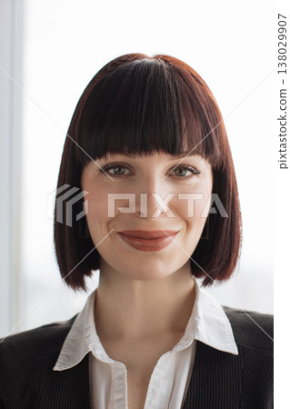 A confident businesswoman with a bob haircut and professional attire smiles warmly, conveying approachability and competence in a corporate setting 138029907