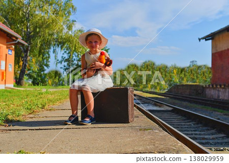 Cute girl holding stuffed animal on a railway station, waiting for the train with vintage suitcase. Traveling, holiday and chilhood concept. Travel insurance concept. Travel, tourism, summer vacation Cute girl holding stuffed animal on a railway station, waiting for the train with vintage suitcase. Traveling, holiday and chilhood concept. Travel insurance concept. Travel, tourism, summer vacation 138029959