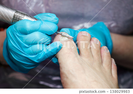 Professional Pedicure Treatment. Nail Technician Using Electric Drill on Toenails in Beauty Salon with Blue Gloves. Care and cosmetic treatment with proper hygiene standards.  138029983