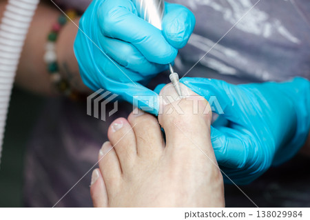 Professional Pedicure Treatment. Nail Technician Using Electric Drill on Toenails in Beauty Salon with Blue Gloves. Care and cosmetic treatment with proper hygiene standards. Professional Pedicure Treatment. Nail Technician Using Electric Drill on Toenails in Beauty Salon with Blue Gloves. Care and cosmetic treatment with proper hygiene standards. 138029984