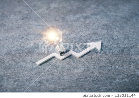 Glowing lightbulb resting on white upward growth arrow illustrates creative thinking for business development, as innovation concept brings success on gray stone surface background Glowing lightbulb resting on white upward growth arrow illustrates creative thinking for business development, as innovation concept brings success on gray stone surface background 138031144