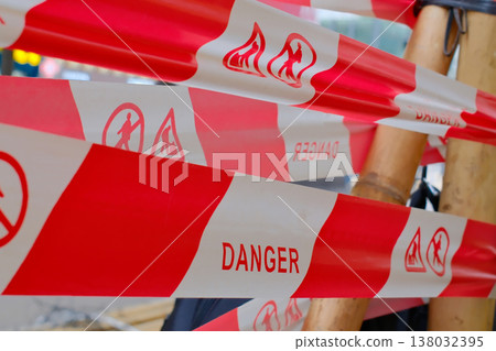 Red and white danger warning barrier tape with hazard symbols on construction site 138032395