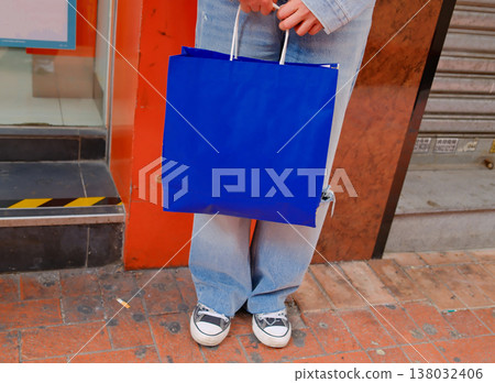 Woman holding bright blue shopping bag standing on Hong Kong urban street sidewalk casual style Woman holding bright blue shopping bag standing on Hong Kong urban street sidewalk casual style 138032406