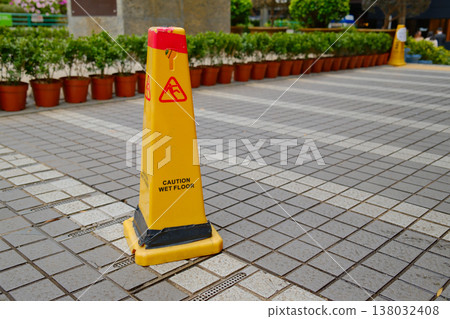 Yellow caution wet floor warning sign on tiled pedestrian walkway 138032408