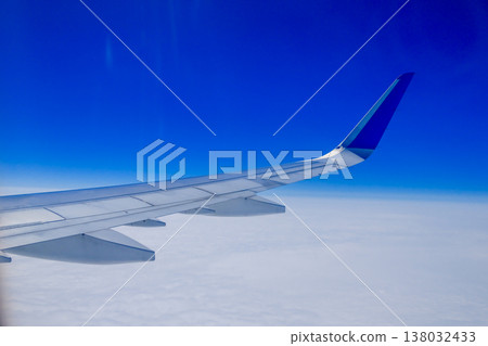 Airplane wing over white clouds with vivid blue sky horizon view from passenger window during flight Airplane wing over white clouds with vivid blue sky horizon view from passenger window during flight 138032433