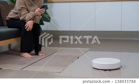Woman controlling a robotic vacuum cleaner Woman controlling a robotic vacuum cleaner 138033788