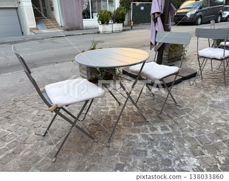 Outdoor cafe table with chairs on cobblestone street. Urban lifestyle, street dining, minimal setup, European city atmosphere Outdoor cafe table with chairs on cobblestone street. Urban lifestyle, street dining, minimal setup, European city atmosphere 138033860