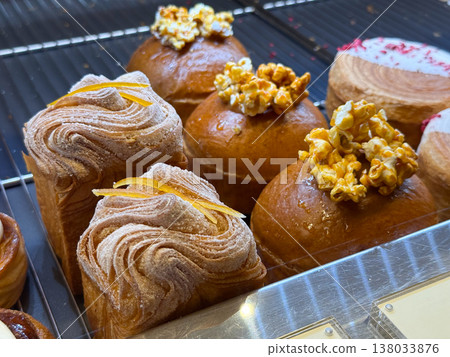 Assorted artisan pastries with caramel popcorn topping and layered cruffins in bakery case. Creative desserts, modern baking, sweet indulgence 138033876