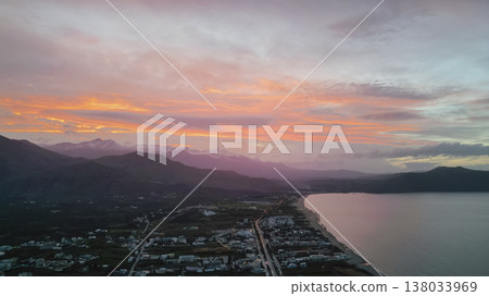 Aerial panoramic view of Crete coastline at twilight with colorful pre-sunset sky, valley with fields and villages, mountain ridge, and reflective sea bay Aerial panoramic view of Crete coastline at twilight with colorful pre-sunset sky, valley with fields and villages, mountain ridge, and reflective sea bay 138033969