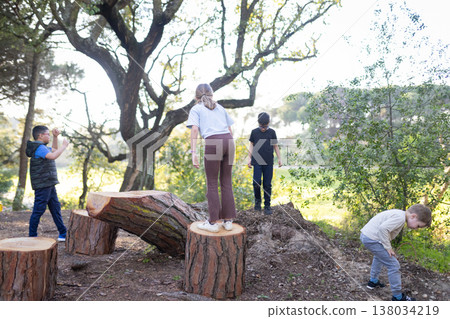 Children playing outdoors on tree stumps and logs Children playing outdoors on tree stumps and logs 138034219