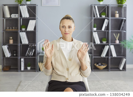 Woman sitting in office room near large shelves with books raising both hands palms facing forward 138034249
