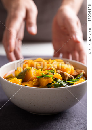 Thai spicy pumpkin curry soup with pork in a bowl with hand serving 138034366