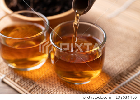 Pouring hot black tea from teapot into a glass cup, Asian healthy beverage culture Pouring hot black tea from teapot into a glass cup, Asian healthy beverage culture 138034410