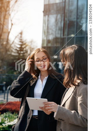 Women discussing business ideas while using a tablet in an outdoor office setting near city buildings during daylight hours 138034504