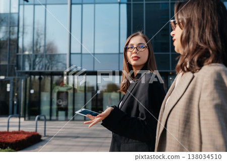 Woman walking in city holding tablet while talking to colleague outside modern office building during business hours 138034510