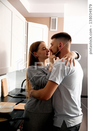 Couple shares a moment in the kitchen while preparing a meal during daytime hours in a cozy home setting 138034979