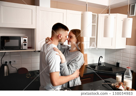 Couple shares a moment in the kitchen while preparing food and enjoying each other's company during a late morning on a weekend Couple shares a moment in the kitchen while preparing food and enjoying each other's company during a late morning on a weekend 138034983