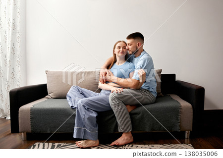 Couple sitting closely on a couch in a living room during a relaxed morning at home, enjoying each others company in comfortable clothing Couple sitting closely on a couch in a living room during a relaxed morning at home, enjoying each others company in comfortable clothing 138035006