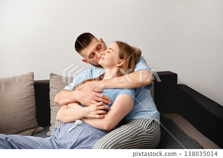 Couple shares a moment of affection while sitting together on a couch in a cozy apartment during the day Couple shares a moment of affection while sitting together on a couch in a cozy apartment during the day 138035014