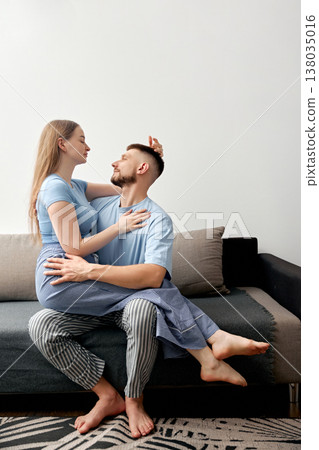 Couple sits together on a couch in a living room, enjoying an intimate moment in casual home attire during the day 138035016