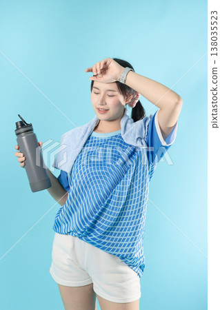 Tired sweat sport woman teen holding a water bottle and a towel standing rest isolated in studio Tired sweat sport woman teen holding a water bottle and a towel standing rest isolated in studio 138035523