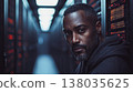 Middle-aged man in charcoal hoodie stands in a bright data center with organized server racks 138035625