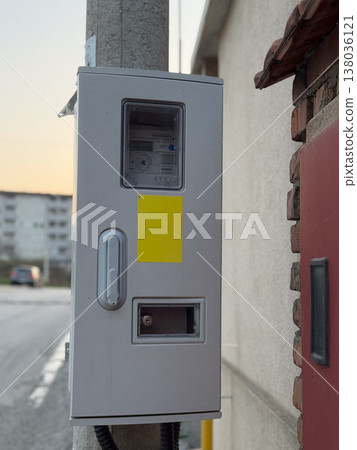Electricity meter box mounted on exterior wall near residential street. Utility infrastructure, energy measurement, consumption monitoring, service connection, urban supply system, household 138036121