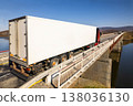 Red truck with white trailer moving on a bridge over the river 138036130