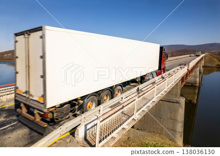 Red truck with white trailer moving on a bridge over the river Red truck with white trailer moving on a bridge over the river 138036130