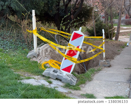 Roadwork excavation site with warning tape and barrier sign on sidewalk. Construction zone, urban maintenance, safety restriction, infrastructure repair Roadwork excavation site with warning tape and barrier sign on sidewalk. Construction zone, urban maintenance, safety restriction, infrastructure repair 138036133