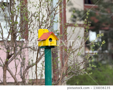 Colorful wooden birdhouse mounted on post in urban yard. Wildlife support, garden decor, handmade object, outdoor environment. Copy space 138036135
