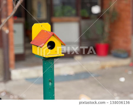 Colorful wooden birdhouse mounted on post in urban yard. Wildlife support, garden decor, handmade object, outdoor environment. Copy space 138036136