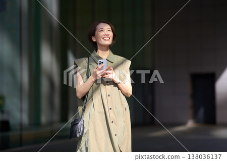 A smiling Japanese woman in casual attire outdoors in the city. 138036137