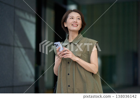 A smiling Japanese woman in casual attire outdoors in the city. 138036142