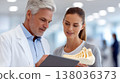 Doctor consulting female patient while examining foot skeleton model and using tablet in modern medical clinic discussing diagnosis and treatment 138036373