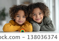 Smiling mixed race twin children with curly hair leaning on table with colorful rainbow toy in cozy home interior 138036374