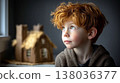 Cute caucasian redhead boy with freckles looking thoughtfully at handmade gingerbread house in cozy home interior 138036377