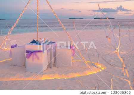 Romantic beach dinner with lights and flowers, ocean view, vibrant colorful sky and clouds, dreamy tropical evening 138036802