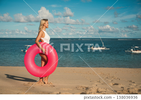 Woman stands on sandy beach holding a float ring Woman stands on sandy beach holding a float ring 138036936