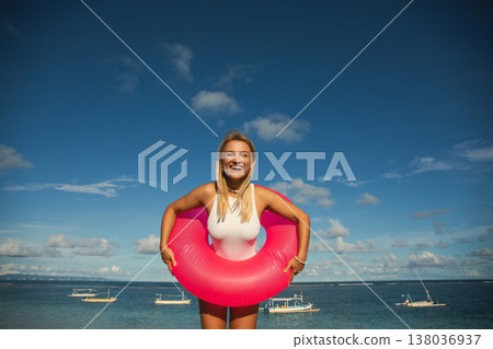 Woman laughs while holding a pink float at the beach 138036937