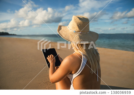 Person using a tablet by the water on a sandy beach 138036939